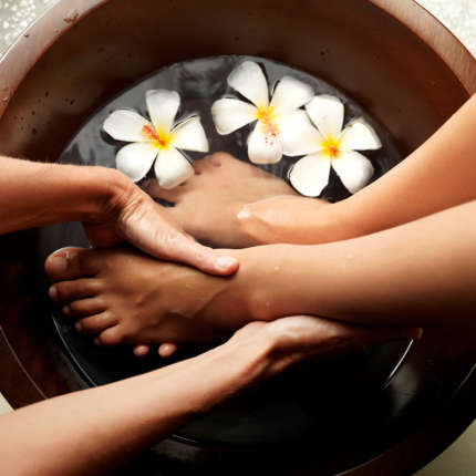 Female feet in foot bath with flowers getting a pedicure